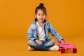 Stylish little child girl with skateboard in denim on orange background Royalty Free Stock Photo