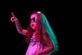 Stylish little girl, beginner fashion model wearing sunglasses posing isolated over dark background in neon light Royalty Free Stock Photo