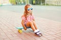 Stylish little girl child sitting on skateboard wearing sunglasses and checkered shirt in city Royalty Free Stock Photo