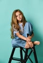 Stylish little girl child wearing summer or autumn jeans clothes sitting on a high chair in the studio.