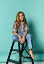 Stylish little girl child wearing summer or autumn jeans clothes sitting on a high chair in the studio.