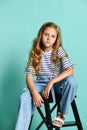 Stylish little girl child wearing summer or autumn jeans clothes sitting on a high chair in the studio
