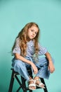 Stylish little girl child wearing summer or autumn jeans clothes sitting on a high chair in the studio.