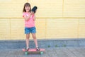 Stylish little girl with a skateboard listens to music on a yellow background Royalty Free Stock Photo