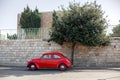 A stylish little red retro car is parked near a tree