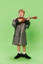 Stylish little school age boy in huge oversize retro style clothes and big male shoes posing with ukulele guitar Royalty Free Stock Photo