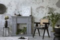 The stylish living room interior with mock up poster, grey fireplace, rattan armchair, concrete wall and dried flowers. Grey