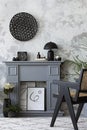 The stylish living room interior with mock up poster, grey fireplace, rattan armchair concrete wall and dried flowers. Grey floor