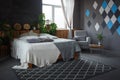 Stylish loft cozy living room with double bed, carpet, armchair, green plants and geometrical patterns on the wall