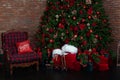 Stylish loft interior of room with Christmas fir tree and checkered armchair. Red sack santa claus with gifts near big Christmas f Royalty Free Stock Photo