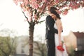 Stylish Loving wedding couple kissing and hugging near tree with blossoms