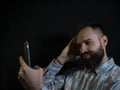 Stylish man with a beard and mustache posing and taking a selfie on the phone on a black background Royalty Free Stock Photo