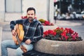 Stylish man with beard in a plaid shirt and jeans in the street near a park with flowers and a guitar in his hands. Macho with a b Royalty Free Stock Photo