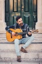 Stylish man with a beard in a plaid shirt and jeans in the street on the steps near the door. Macho with a beautiful smile sits in Royalty Free Stock Photo