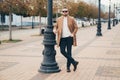 Stylish man with beard standing on street in brown coat with sunglasses.