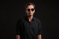 Stylish man a black shirt and sun glasses isolated over black background. Low key portrait. Royalty Free Stock Photo