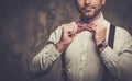 Stylish man with bow tie wearing suspenders and posing on dark background.