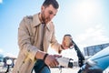 Stylish man with coffe cup in hand inserts plug into the electric car charging socket. Royalty Free Stock Photo