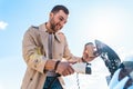 Stylish man with coffe cup in hand inserts plug into the electric car charging socket. Royalty Free Stock Photo
