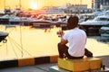 Stylish man and his dog sitting together on pier and enjoying colorful sunset. Royalty Free Stock Photo