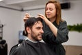 Handsome blue eyed man sitting in barber shop. Hairstylist Hairdresser Woman cutting his hair. Female barber Royalty Free Stock Photo