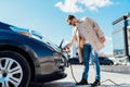 Stylish man in sunglasses disconnects the charging cable from his electric car.