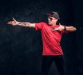 Stylish man with a tattoo on his hand dressed in a hip-hop style, posing for a camera. Studio photo against a dark wall Royalty Free Stock Photo