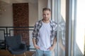 Stylish man wearing checked shirt standing near window