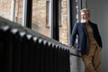 Stylish mature man in business casual wear looking out a large window, being thoughtful while standing in loft interior Royalty Free Stock Photo