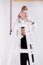 Stylish man is having fun with cute child baby girl in decorated studio. daughter tries to climb the ladder. Love parenthood