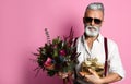 Stylish middle-aged bearded man with a modern haircut, sunglasses and fashionably dressed holds a bouquet of flowers and a gift. Royalty Free Stock Photo