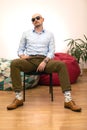 Stylish middle-aged man sitting on black chair. Black glasses add some seriousness to his face.