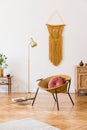 Stylish and minimalist interior of living room with design gold armchair, lamp, poster frames. dressing table with mirror, plants.