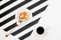 Minimalistic workspace with cup of coffee, bakery, isolated on striped black and white background. Flat lay style Top view. Royalty Free Stock Photo