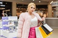 Stylish model glamorous young blonde woman in fashionable luxurious outfit with shop bags stands in shop. Portrait trendy sexy Royalty Free Stock Photo