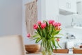 Stylish and modern boho, scandi interior of open space white kitchen with pink tulip flowers in vase on the wooden Royalty Free Stock Photo