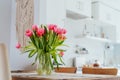 Stylish and modern boho, scandi interior of open space white kitchen with pink tulip flowers in vase on the wooden Royalty Free Stock Photo