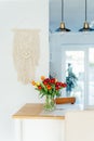 Stylish and modern boho, scandi interior of open space white kitchen with tulip flowers in vase on the wooden kitchen