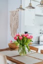 Stylish and modern boho, scandi interior of open space white kitchen with tulip flowers in vase on wooden kitchen Royalty Free Stock Photo