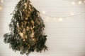 Stylish modern christmas tree made of fir branches, hanging on white wall with festive garland light. Eco Zero waste decoration of Royalty Free Stock Photo