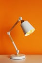 Stylish modern desk lamp on white table near orange wall