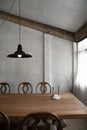 Stylish modern loft dining area with natural light scene and bare concrete wall with natural wood table and chairs setting /