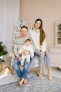 Stylish modern portrait of a young family with a small child. Happy close-knit family sitting near the Christmas tree on a chair Royalty Free Stock Photo