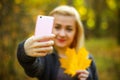 Portrait of cheerful young woman with autumn leafs in front of foliage making selfie Royalty Free Stock Photo