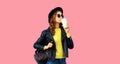 Stylish modern young woman drinks coffee wearing black rock leather jacket, sunglasses, round hat on pink studio background Royalty Free Stock Photo