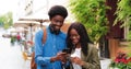 Stylish multiracial man and his girlfriend using his smartphone while walking down the street. Handsome man chatting