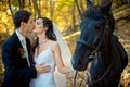 Stylish newlywed couple kissing during their walk with horse along the autumn forest. Romantic wedding portrait. Royalty Free Stock Photo