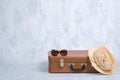 Stylish old fashioned accessories of hipster female traveller: vintage sunglasses, straw hat, leather suitcase on grey background. Royalty Free Stock Photo