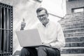 Stylish old man working on laptop surfing the internet sitting on stairs outdoors city in digital nomad Senior using modern Royalty Free Stock Photo