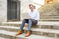 Stylish old man working on laptop surfing the internet sitting on stairs outdoors city in digital nomad Senior using modern Royalty Free Stock Photo